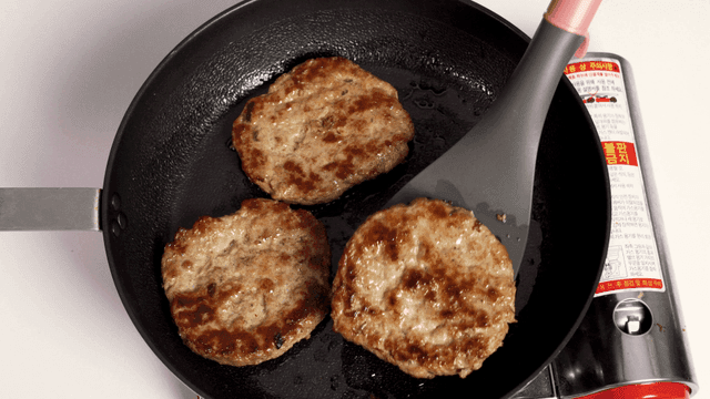 Three patties cooking in a frying pan