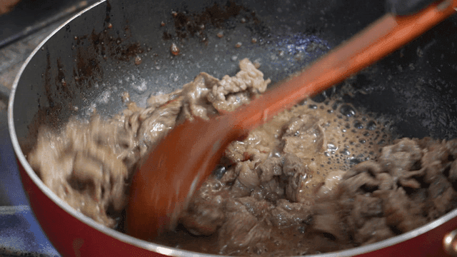 Stir-fry meat in pan with wooden spatula
