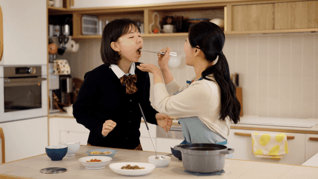 Mother feeding her daughter side dishes in kitchen