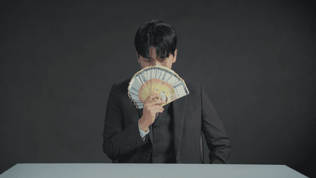 Man smiling with his mouth covered by money