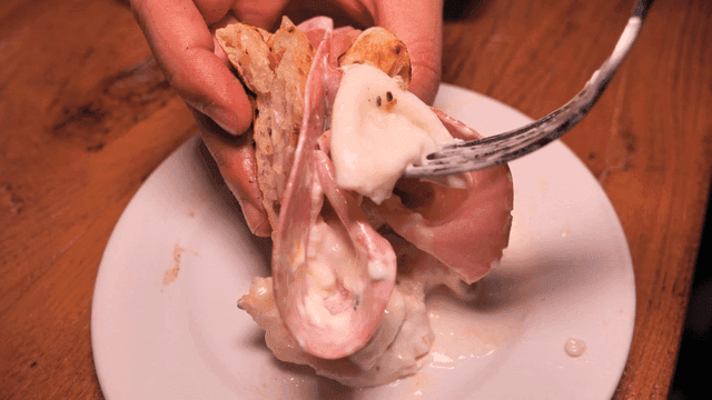 Hand picking up mortadella pizza with fork