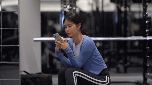 Young woman sitting in a gym using her phone