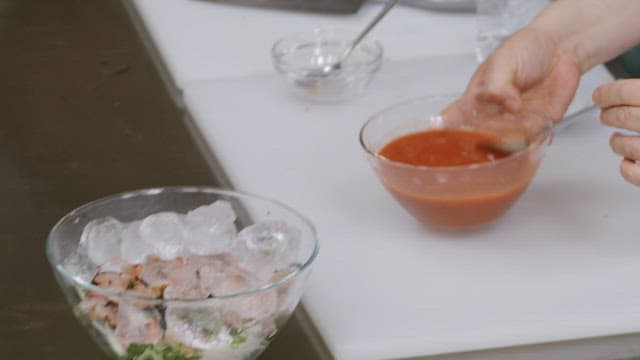Pouring sauce into a bowl containing ice, vegetables, and conches