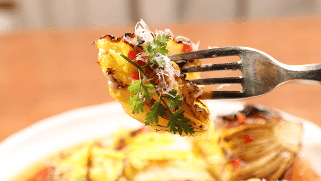 Fork lifting roasted cabbage with herbs and sauce