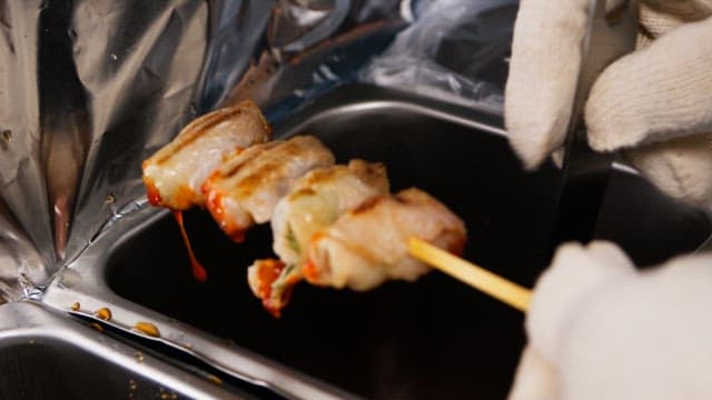 주방에서 꼬치구이에 소스를 바르는 장갑 낀 손