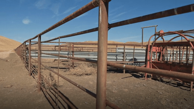 A dry field with a metal fence and hills