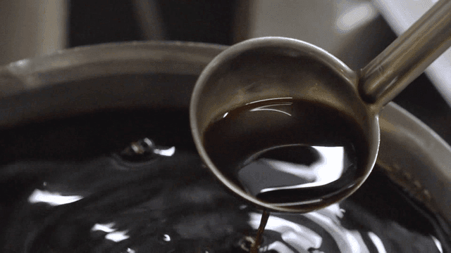 Ladle scooping rich soy sauce from large pot