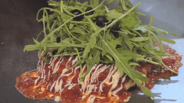 Okonomiyaki decorated with arugula and sauce