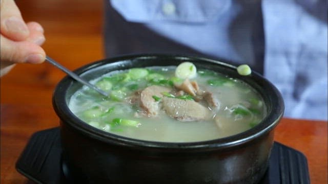 Person stirring a bowl of ox bone soup with spoon