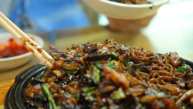 Chopstickful of seafood Jjajang noodles on an iron plate with steaming hot sauce