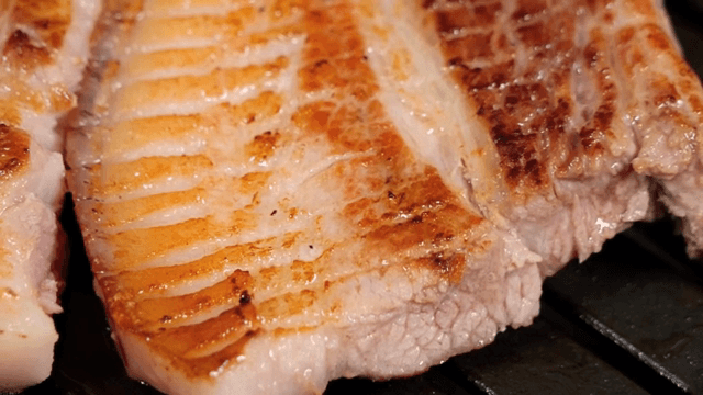 Grilled pork shoulder sizzling on a pan
