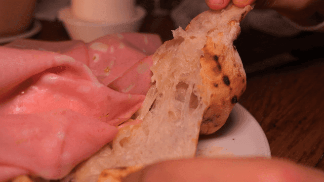 Scene of tearing pizza from wood-fired oven by hand