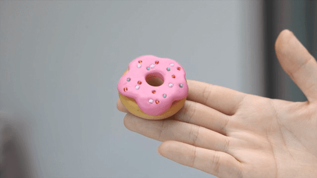 A hand holding a small pink donut made of clay