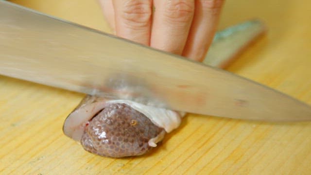 Raw fish being cut with a knife on a wooden cutting board