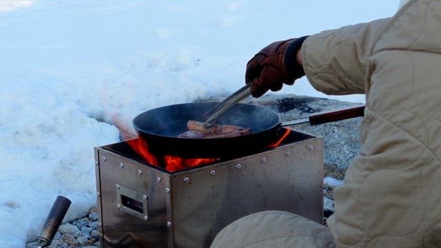 Fresh lamb being cooked on a portable stove in snowy outdoors