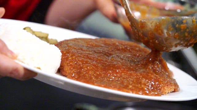 Sauce being poured over a crispy pork cutlet