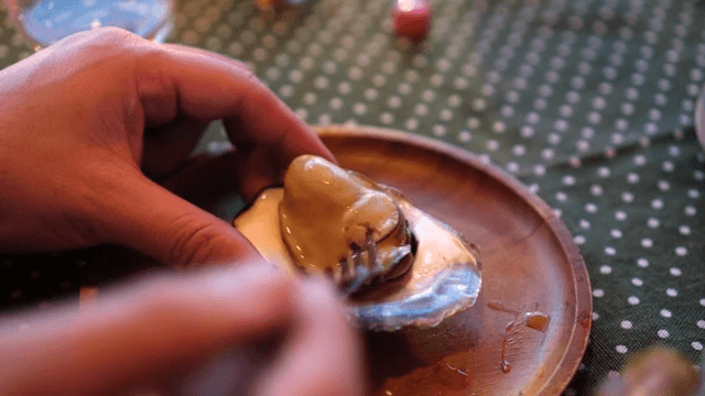 나무 접시 위에 놓인 굴에 소스를 뿌려 먹는 모습