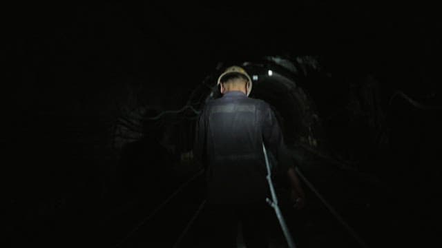 Back of miner walking inside a dark coal mine tunnel, illuminated by dim lights