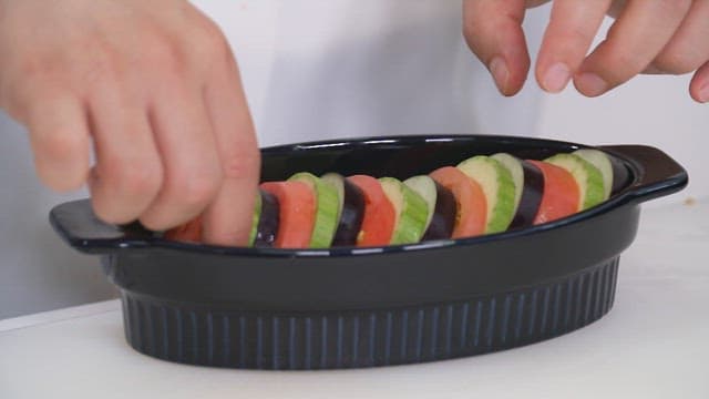 주방에서 검은 오븐 접시에 놓이는 토마토와 호박, 가지