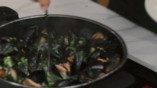 Mussel soup being with vegetables ladled into a white bowl