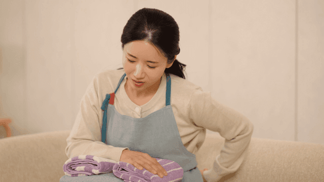 Woman experiences back pain while folding laundry on sofa