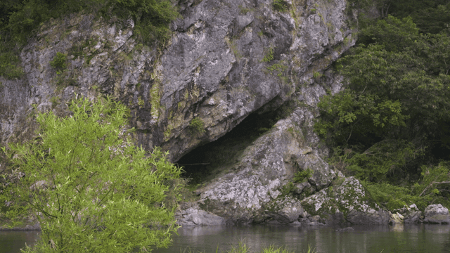 Entrance to rock cave by quiet river