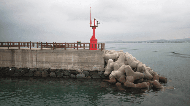 Red lighthouse on concrete pier by sea