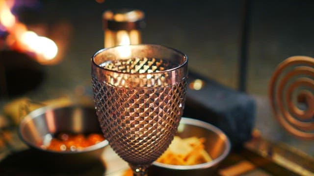 Camping of a filled wine glass with snacks around the table next to a warm fire