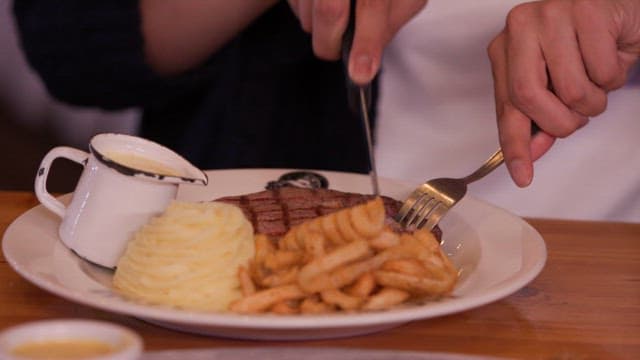 Person cutting steak with mashed potatoes and fries