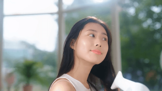 햇빛이 비치는 실내에서 헤어 드라이어로 머리를 말리는 여성