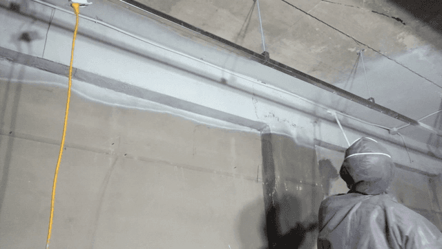 Worker painting ceiling with long spray gun