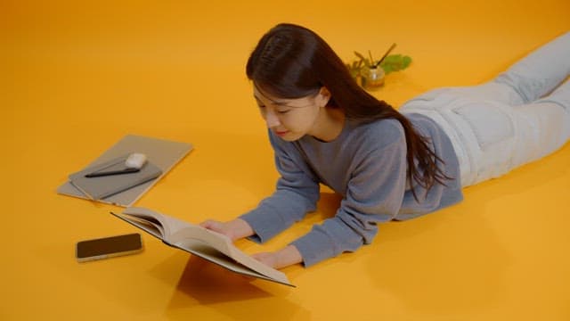 밝은 방에서 배를 깔고 누워서 책을 읽는 여성