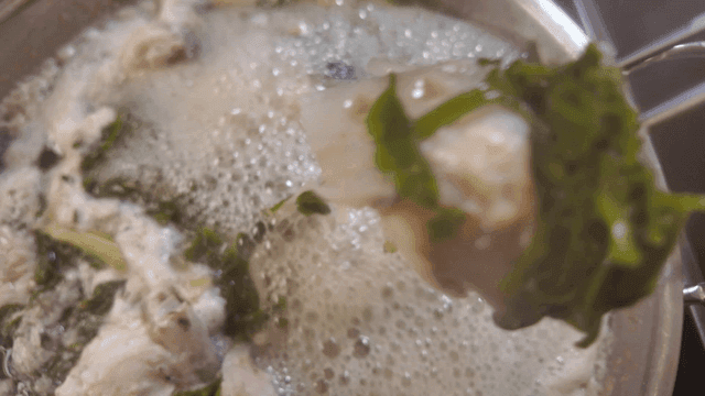 Chopsticks holding fish in anglerfish stew boiling with vegetables