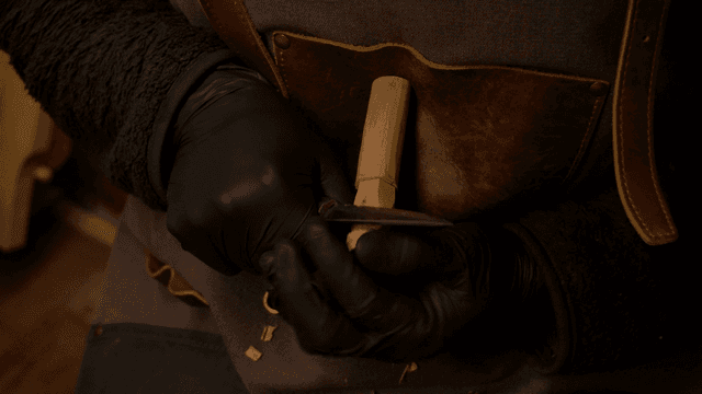 Artisan carving a wooden piece against his chest with a precise knife