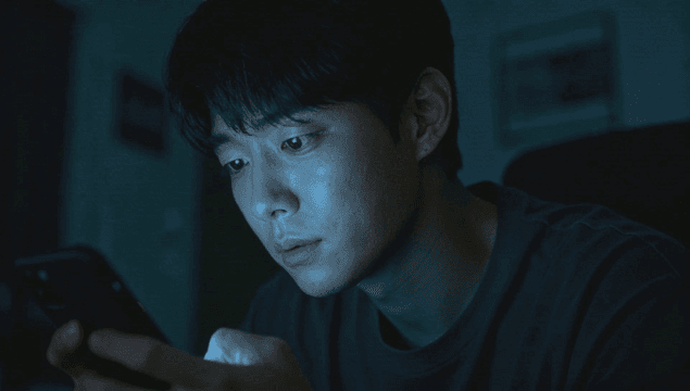 어두운 방에서 스마트폰을 집중하여 사용하는 남성
