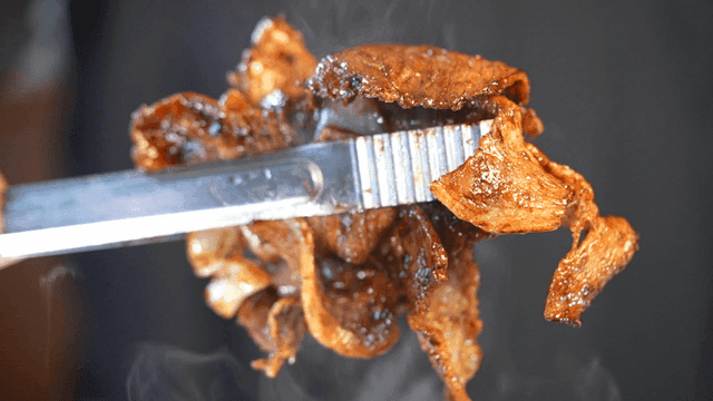 Grilled stir-fried pork held with tongs