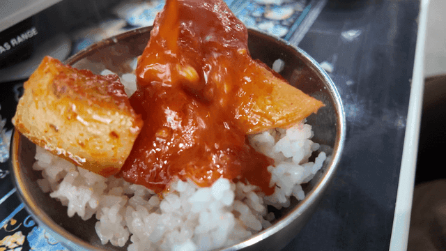 Ladle with spicy chicken stew potatoes and carrots on top of rice