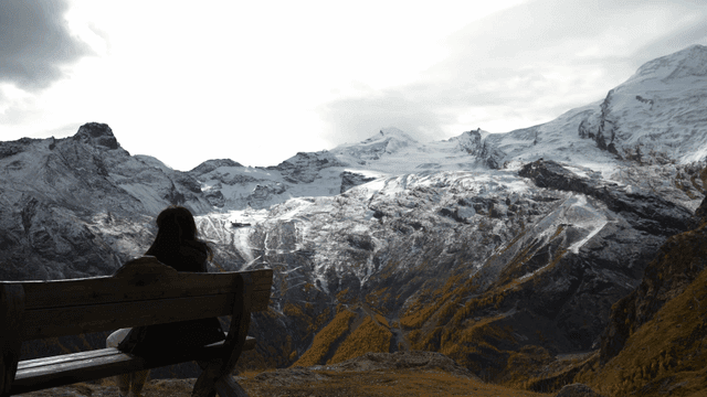 Back view of woman sitting on bench looking at snow-covered mountain