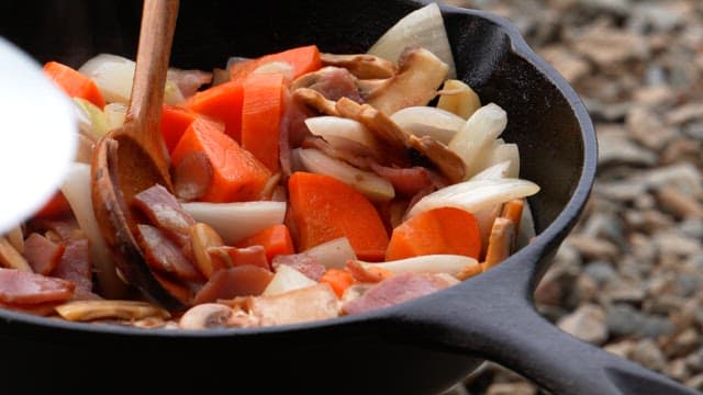 Stir-frying various vegetables and bacon in a heated frying pan