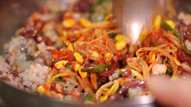 Mixing Korean beef tartare bibimbap with a spoon in a bowl