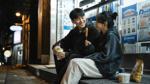 Couple eating hot dog and drink outside convenience store at night