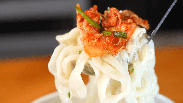 Ladle of chicken kalguksu topped with kimchi