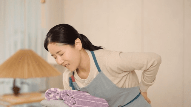 Woman experiencing back pain while folding laundry