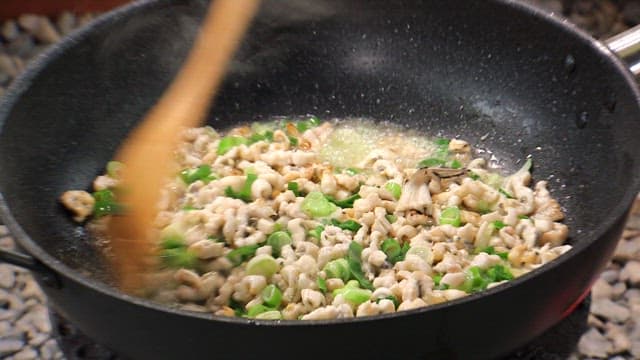 Cooking seafood in a frying pan with trimmed eel and green onions