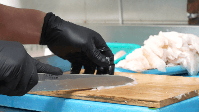 Hands slicing fresh fish fillets on cutting board