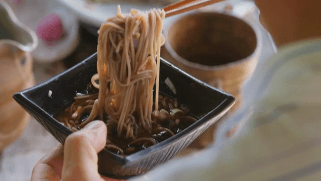 Chopsticks lifting soba noodles from a bowl