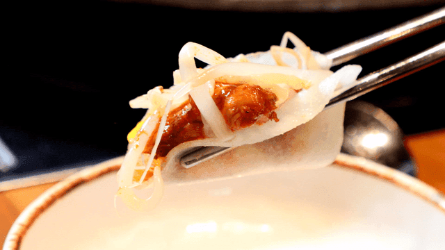 Spicy chicken wrapped in ssammu picked up with chopsticks