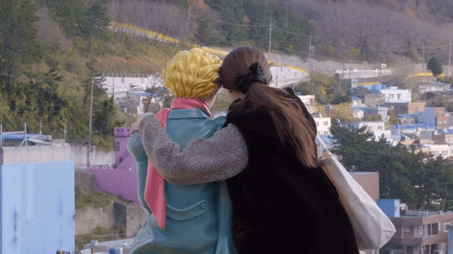 언덕 마을을 내려다보는 조각상과 사진 찍는 여성