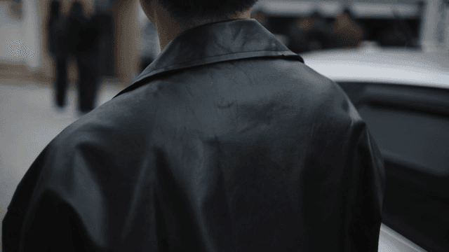 Back view of man in leather jacket approaching people