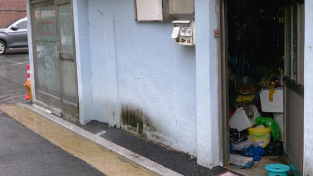 Narrow alley with cluttered items outside the door under a light rain